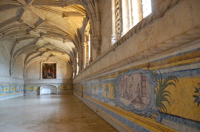 A wide hall with stone floors, vaulted ceilings, and colorful old mosaics decorating the walls.