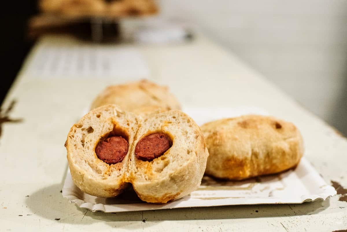 Two bread rolls on a small white plate, one of which has been cut open to reveal the filling of chorizo inside.