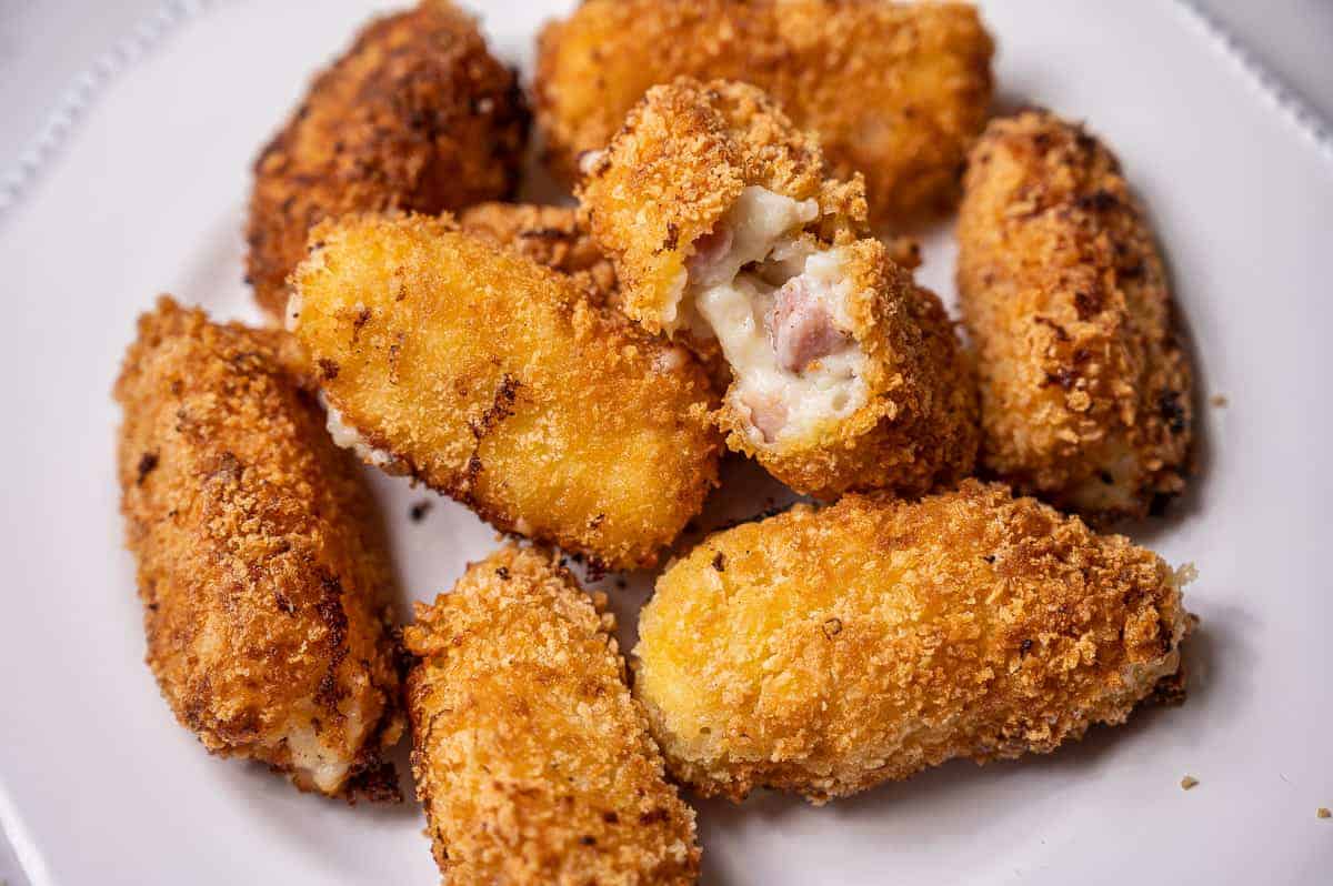 Several crispy Spanish ham croquettes on a white plate, one broken in half.