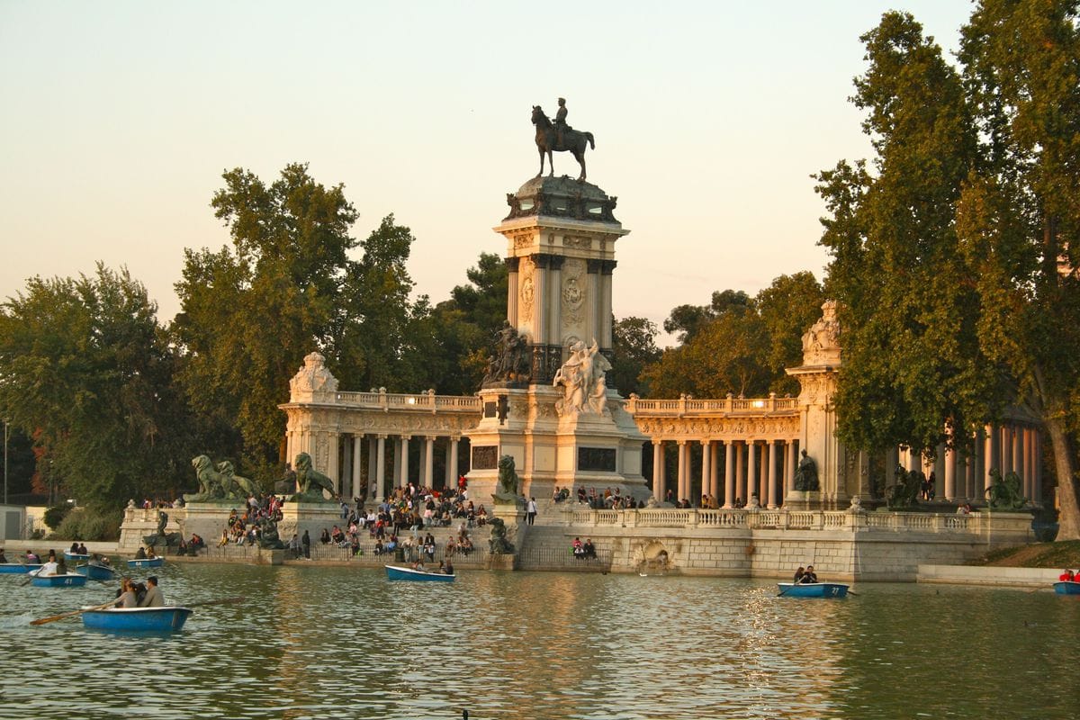 Retiro's lake at sunset, with blue rowboats and a large statue and columns on one side.