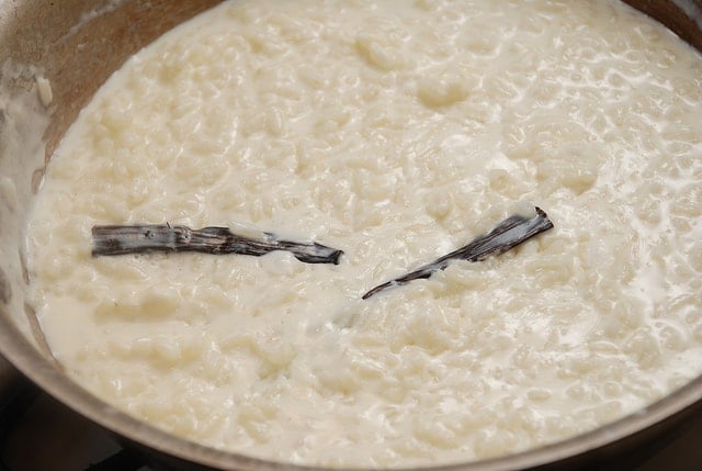 Close-up of a pot of creamy white rice pudding with two sticks of vanilla.