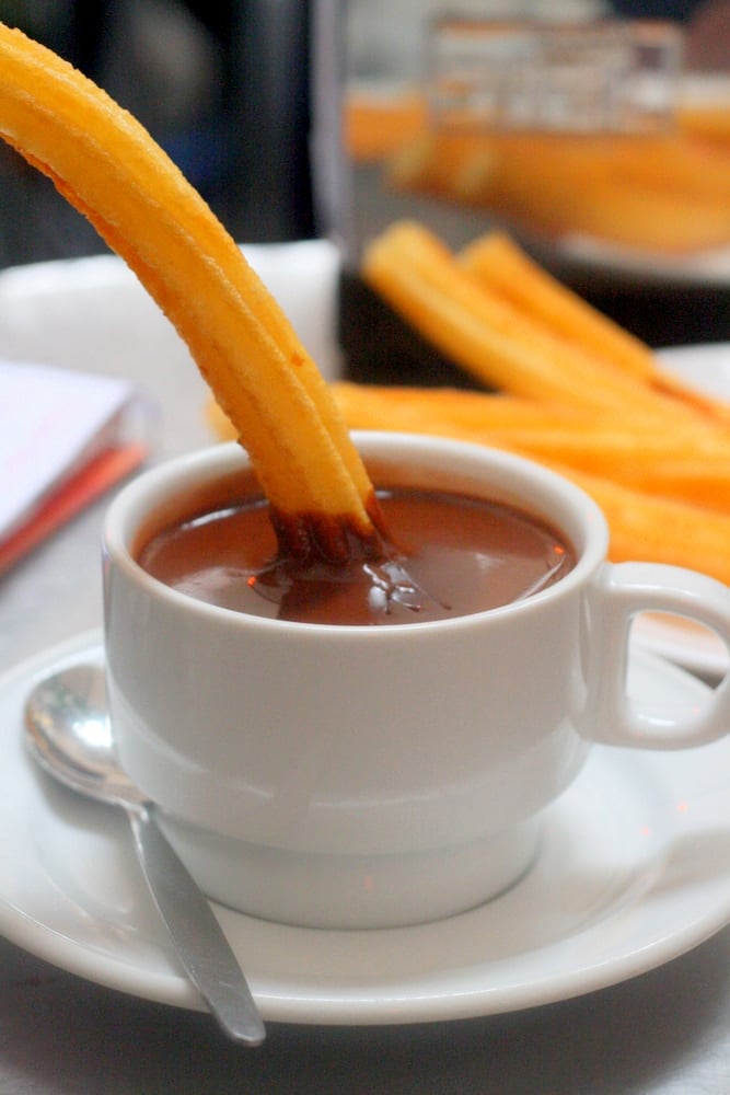 Close-up of a thin churro being dipped into a white mug of thick hot chocolate.