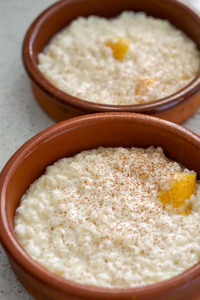 Two servings of arroz con leche (Spanish rice pudding) in round clay dishes.