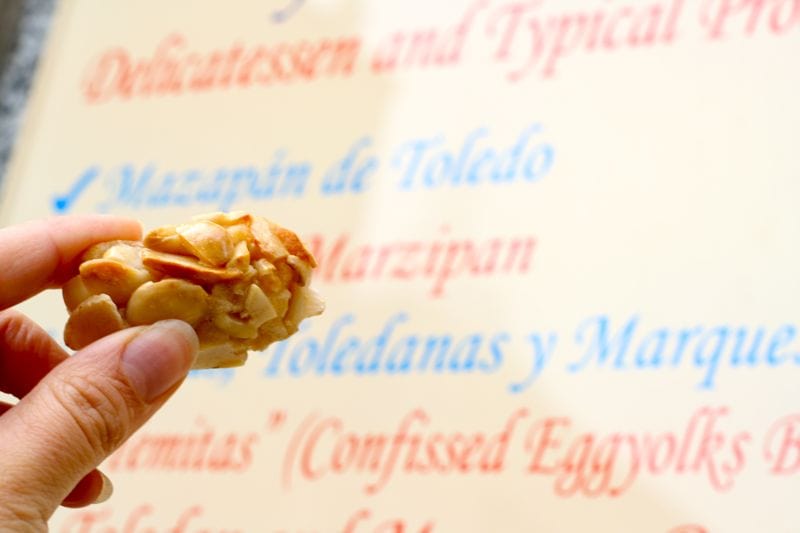 Close-up of someone holding a small piece of almond-coated marzipan with a menu behind it.