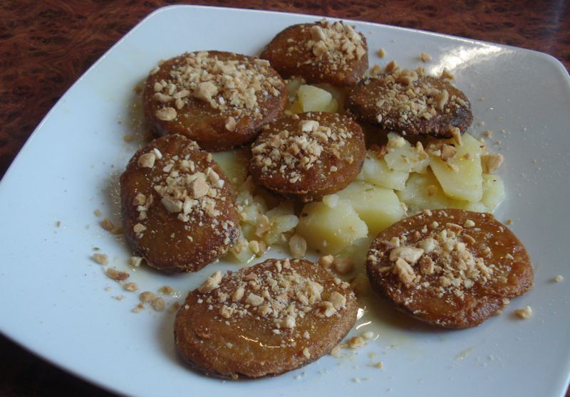 A plate of fried eggplant slices topped with honey and crumbled almonds.