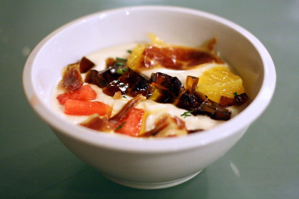 A bowl of white ajo blanco soup with colorful toppings.