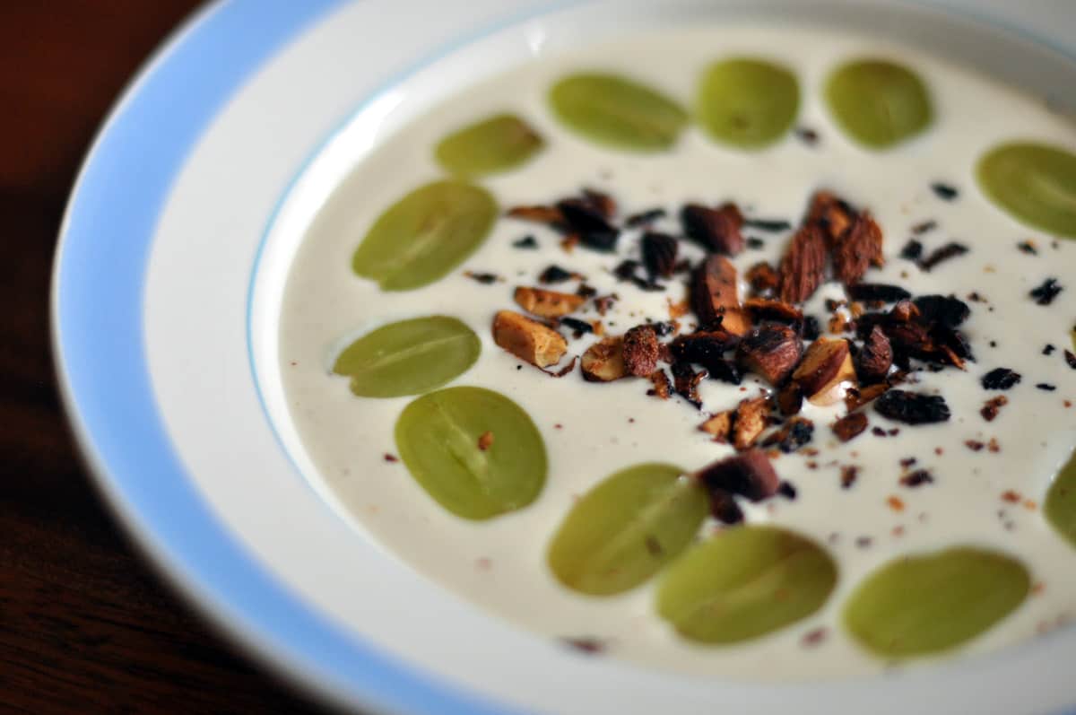 Bowl of chilled garlic soup garnished with white grapes and other toppings served as a vegetarian tapa.