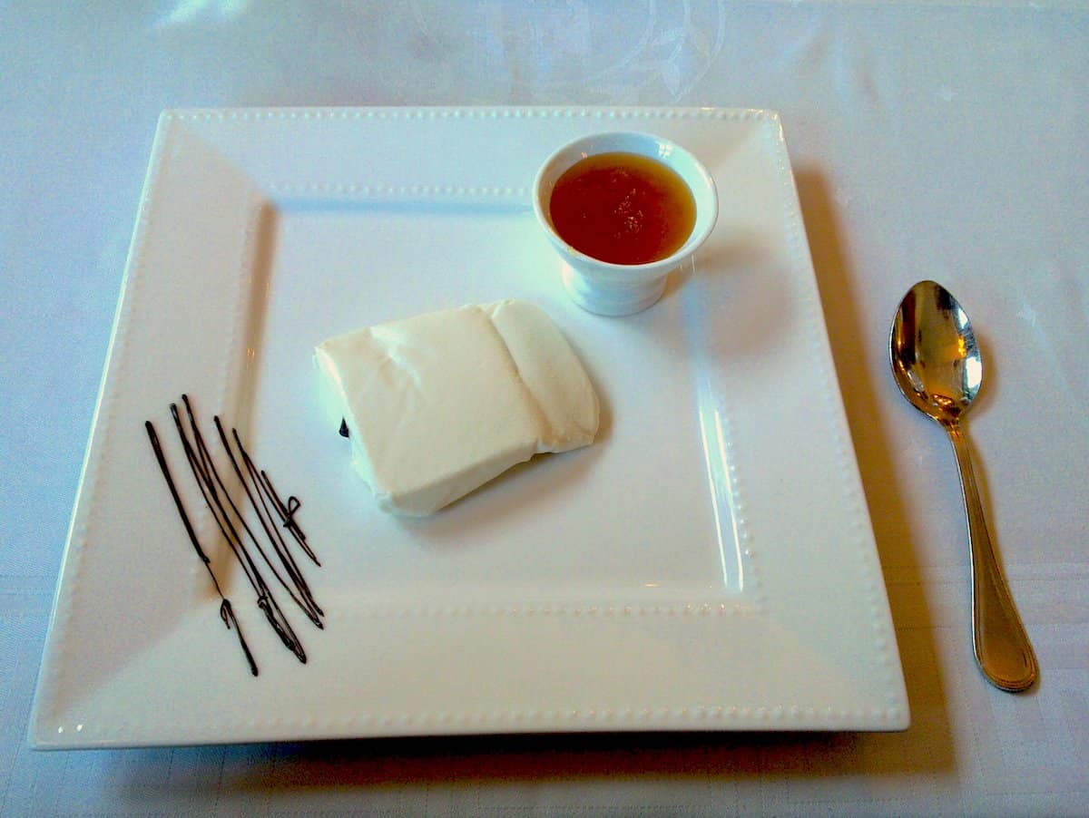 A large square plate with a piece of fresh cheese and a small cup of honey.