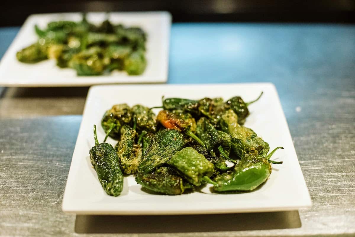 Two plates of small fried green peppers, a great vegetarian tapa.