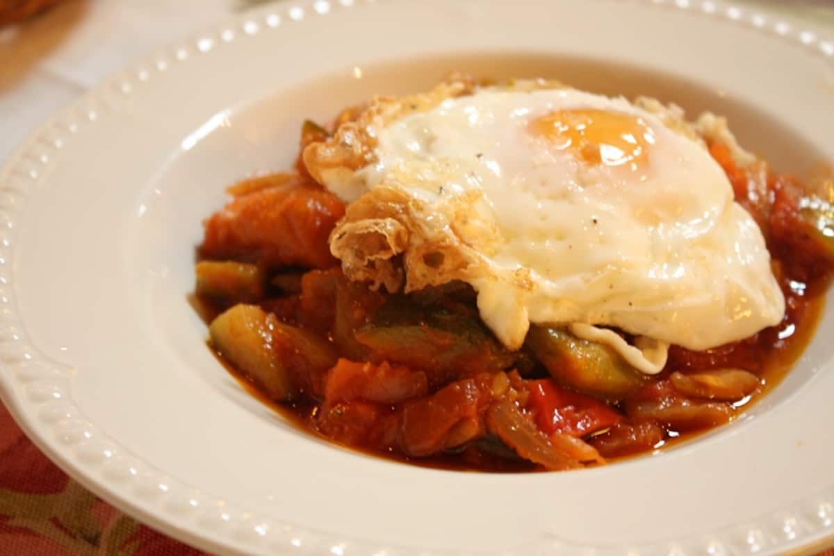 Close-up of slow-simmered tomato and vegetables topped with a fried egg.