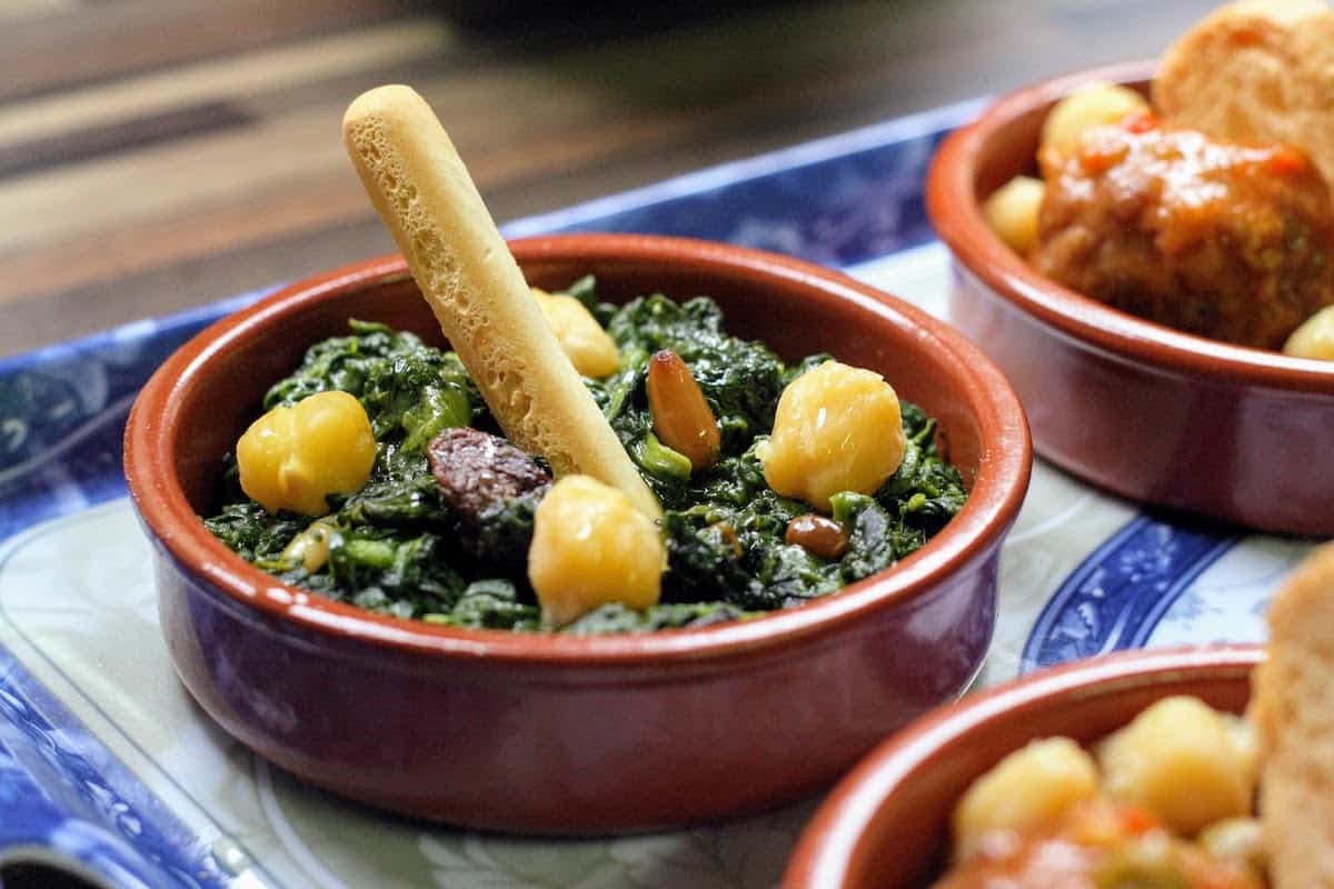 Small clay dish of sauteed spinach with raisins and toasted pine nuts, a traditional vegetarian tapas recipe.