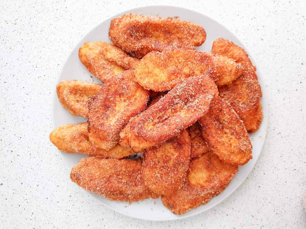 Overhead view of cinnamon-sugar-coated Spanish torrijas piled on a white plate.