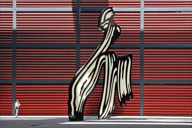 An enormous abstract statue resembling black and white paint strokes, with a red wall behind it.