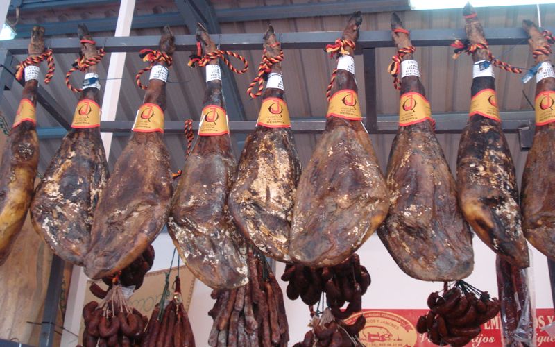 Legs of cured Spanish ham hanging from a metal beam, with multicolored ropes around the hooves.