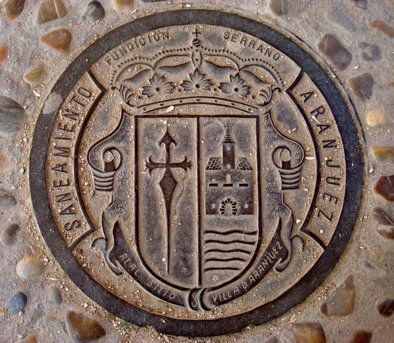 Round engraving in the street depicting the Aranjuez coat of arms, with a cross and building.