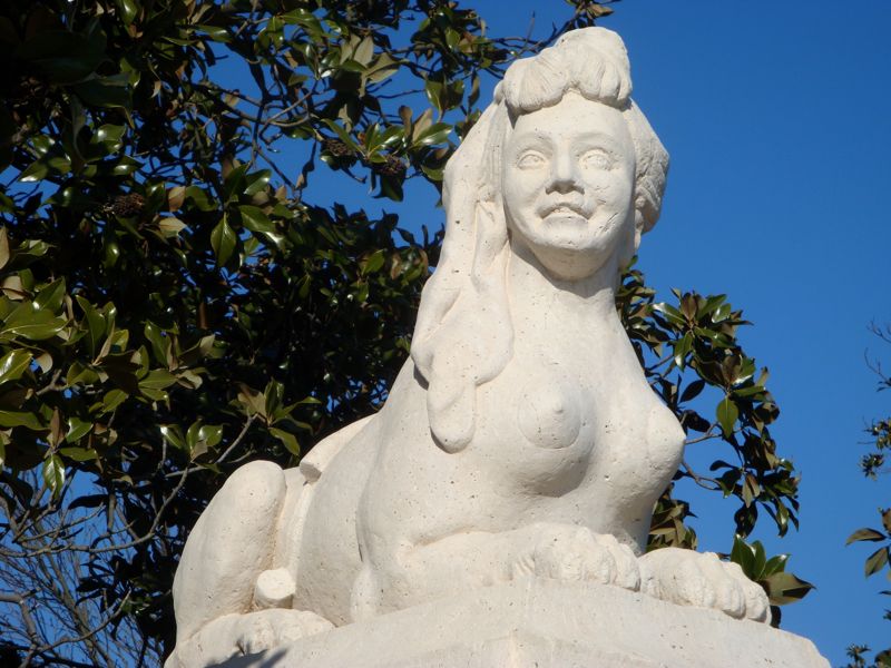 White statue of a sphinx with a woman's head and torso.