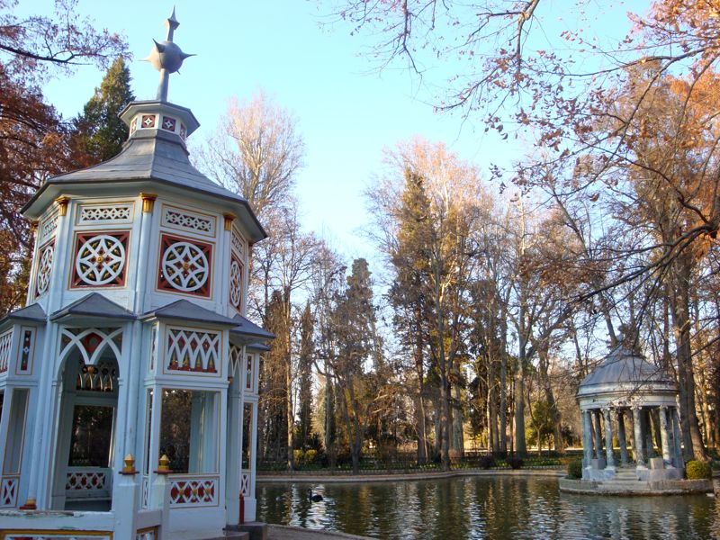 A lake with two small gazebos, one brightly painted, and autumn leaves in the background.