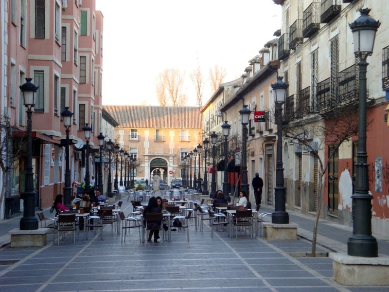 Wide pedestrian street with café tables set out across it and old buildings on both sides.