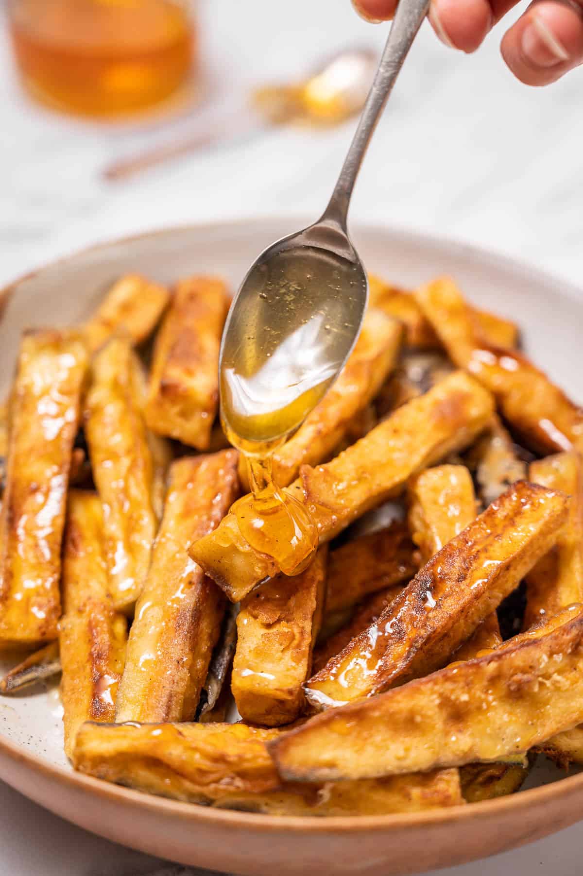 Honey being drizzled over fried eggplant slices with a metal spoon.