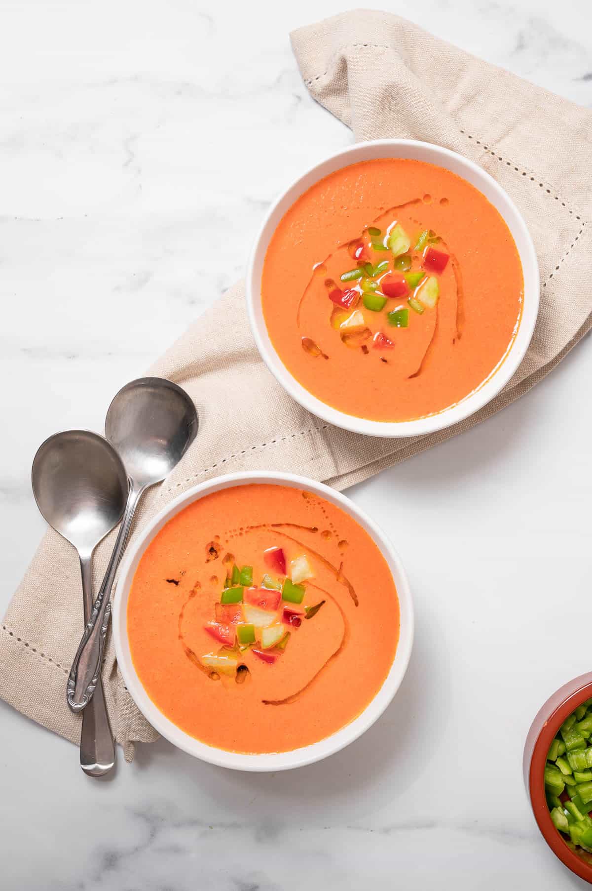 Spanish authentic gazpacho recipe served in two white bowls and topped with chopped vegetables.