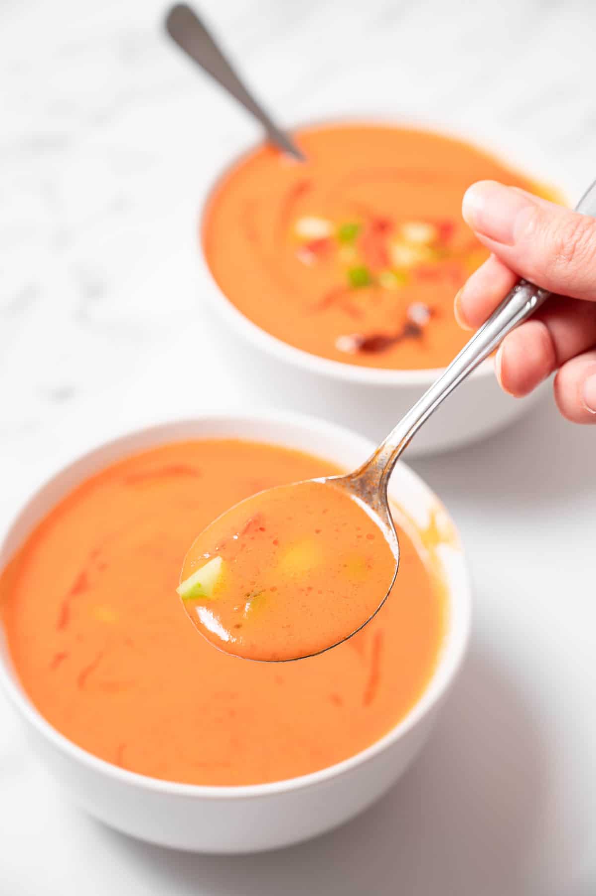 A spoonful of cold traditional gazpacho from a white bowl.