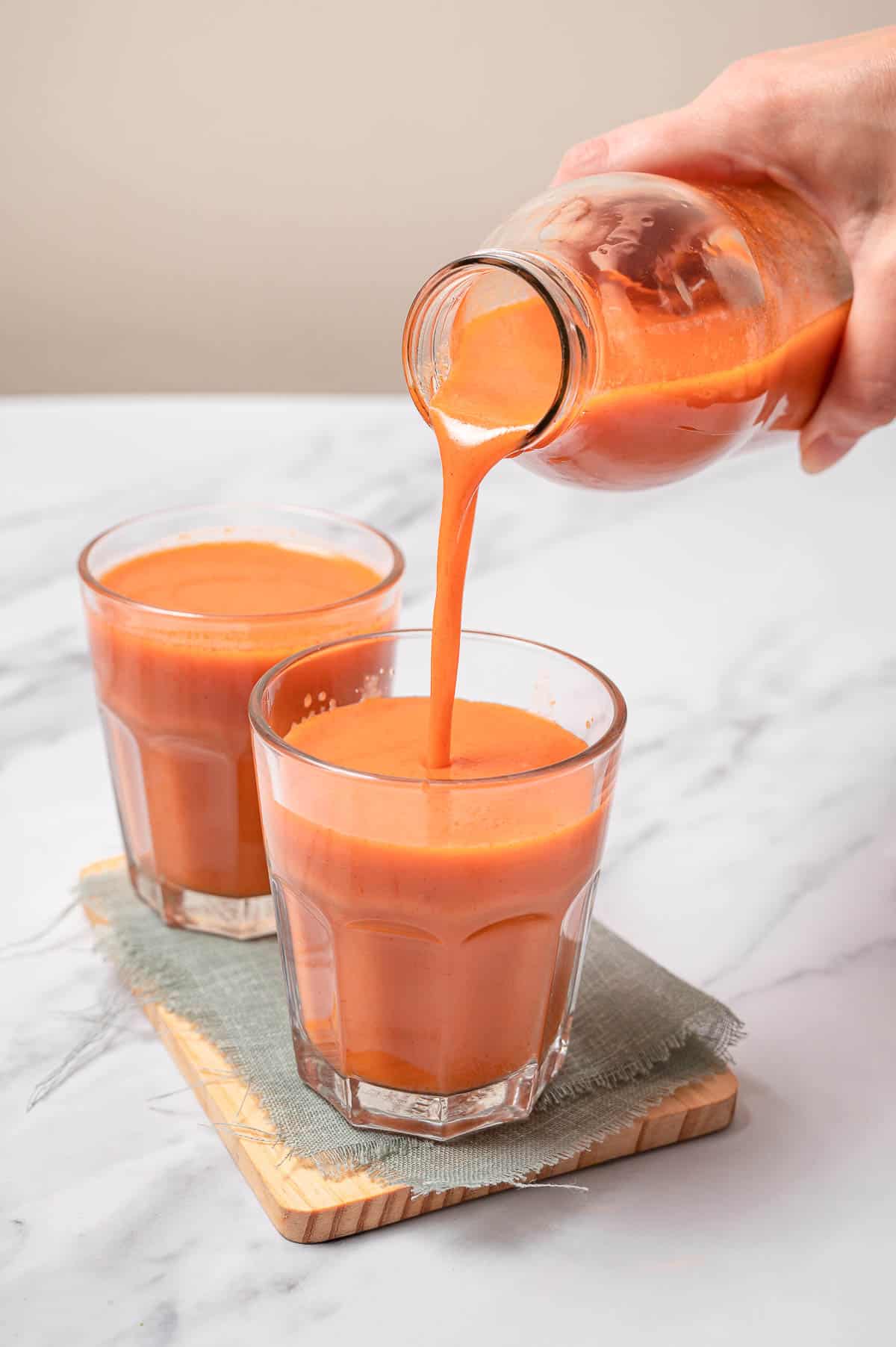 Spanish authentic gazpacho poured from a glass pitcher into two small glasses. 