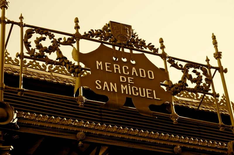 Sepia-tone photo of the ornate iron sign for San Miguel Market in Madrid.