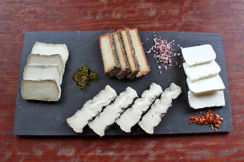 A slate cheese board with four slices each of four types of cheese, plus colorful garnishes.