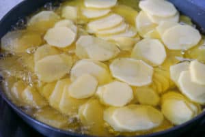 Sliced potatoes in a frying pan covered with olive oil