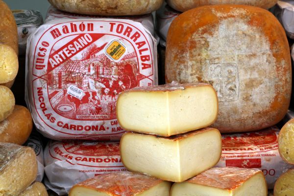 Close-up of several square blocks of Mahón cheese, with two large wedges stacked in front. 