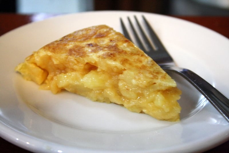 A slice of Spanish potato omelet with a soft center and golden-brown top on a plate.