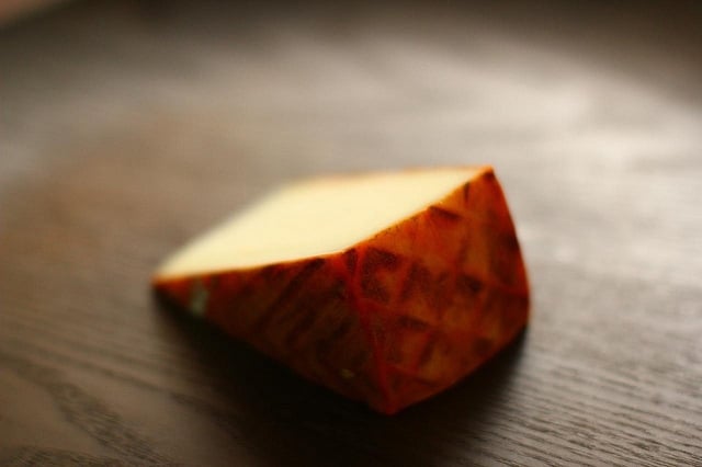 Close-up of a wedge of cheese with a dark orange rind sitting on a wooden surface.