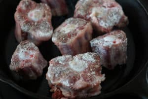 Oxtail coated in flour searing in a cast iron pan