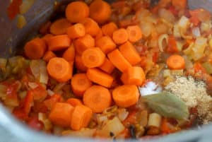 Chopped carrots, bay leafs, and onion, leek, red pepper sauté in a large pot