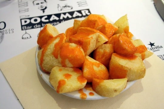 A small plate of fried potato chunks covered in bright orange sauce.