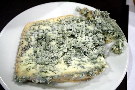 A large slice of crumbly cheese with bright green mold speckled throughout.