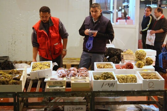 Boxes of products for sale at Mercamadrid, with two men standing behind them.