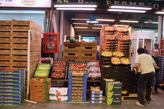 Several boxes of different kinds of fruit stacked high, with a man inspecting them.