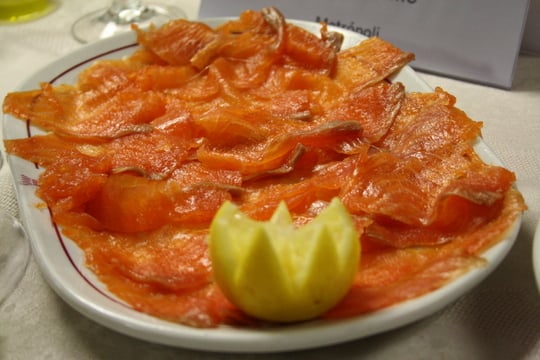 A large plate of sliced smoked salmon with half a lemon.