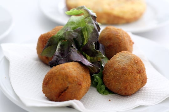 Close-up of four spherical croquettes on a white napkin with a piece of lettuce.