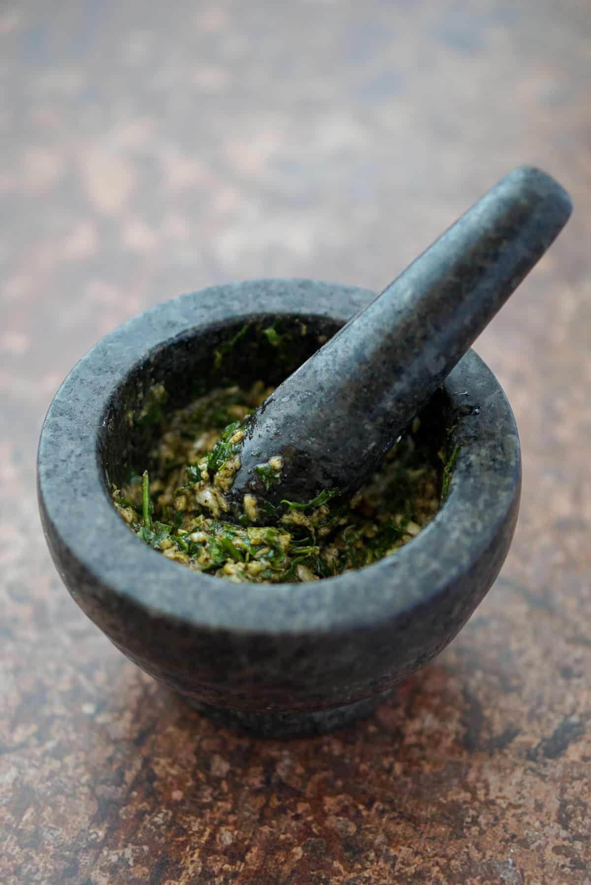 Mortar and pestle with garlic, salt, pepper, and parsley.