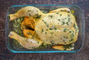 Raw whole chicken in a clear roasting dish with white wine and a stock cube.