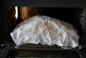 Whole chicken covered in parchment paper in a small oven.