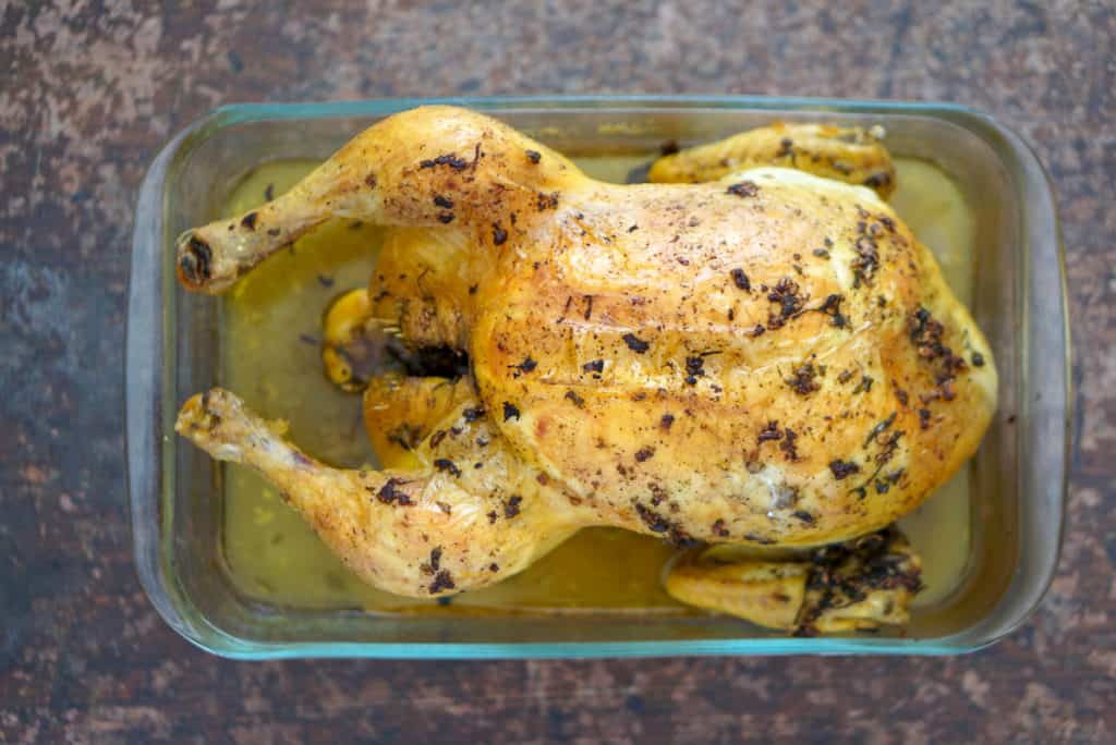 Overhead shot of roasted Spanish whole chicken in a roasting pan with crispy golden skin and juice in the pan.