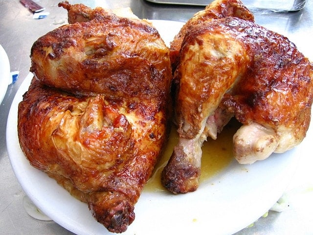 Close-up of two large pieces of roasted chicken with golden-brown skin on a white plate.