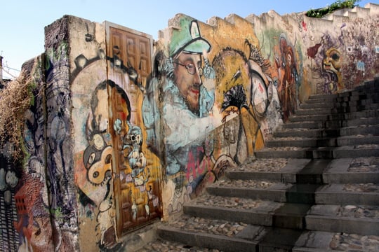 A wall full of colorful murals and street art beside a cobblestone staircase