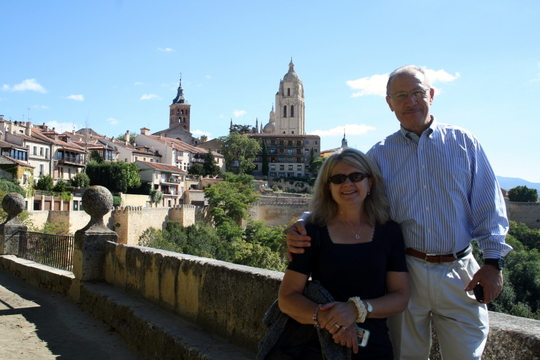 An older couple smiling in front of a panoramic view of Segovia.