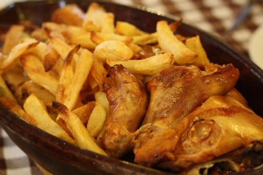 A large dish of golden brown roasted suckling pig and fried potatoes.
