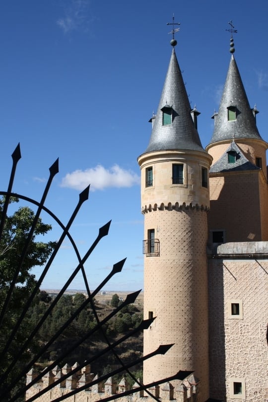 Two turrets of Segovia's medieval castle, with curved iron spikes in the foreground.