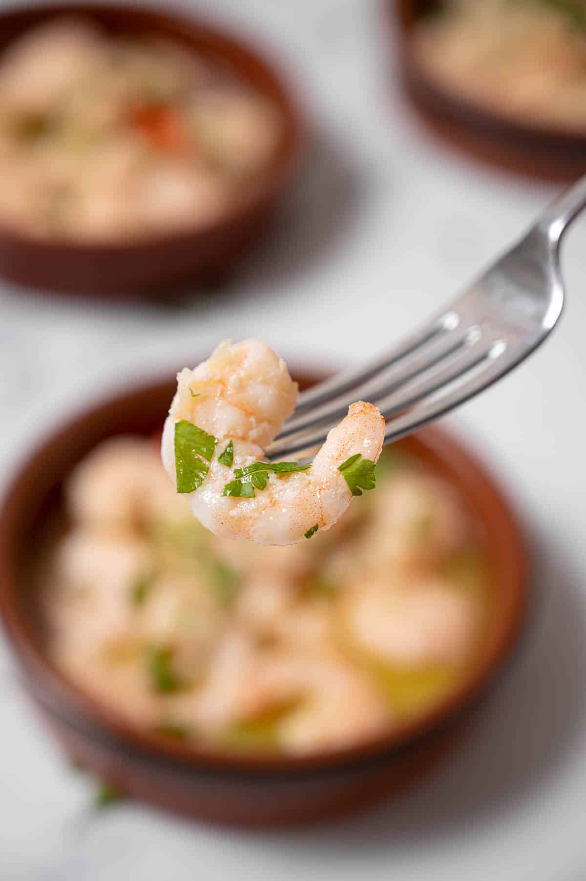 Close up of a garlic shrimp in front of a clay dish of gambas al ajillo